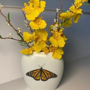 A vase with yellow flowers and a butterfly on it.