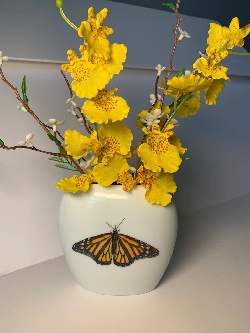 A vase with yellow flowers and a butterfly on it.