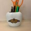 A butterfly is sitting on the side of a white cup.